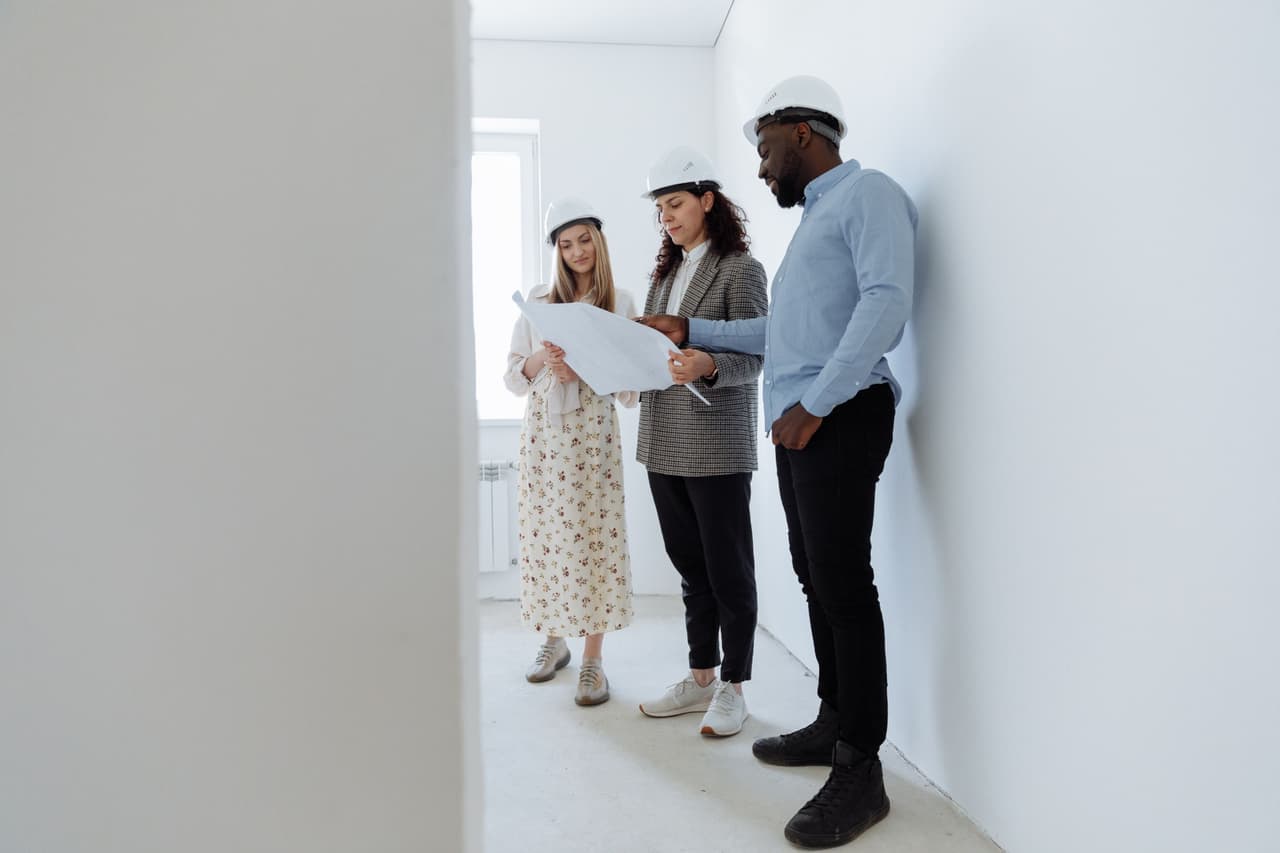 Three people in hard hats reviewing a floor plan in a newly plastered room
